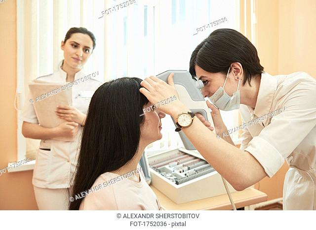 Nurse looking at optometrist examining female patient at hospital