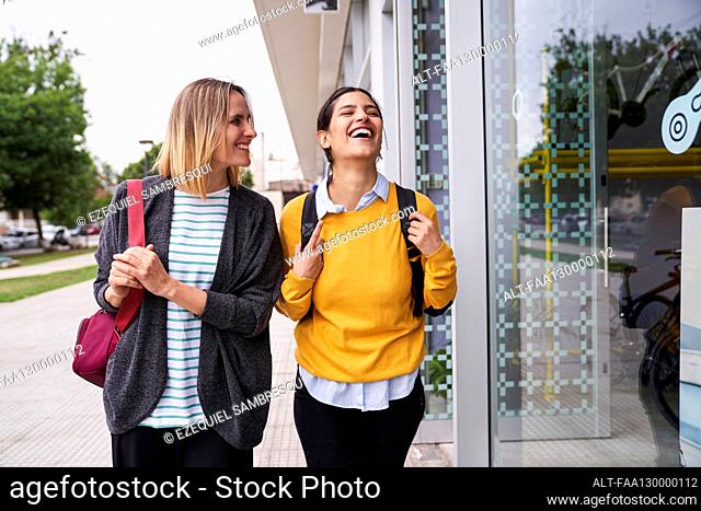 Mid-shot photo of two female friends having a good time outdoors while window shopping