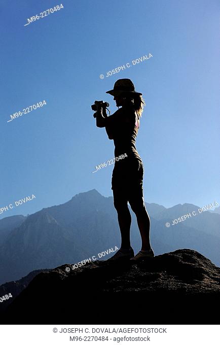 Woman standing on rock with binoculars, Alabama Hills, California, USA