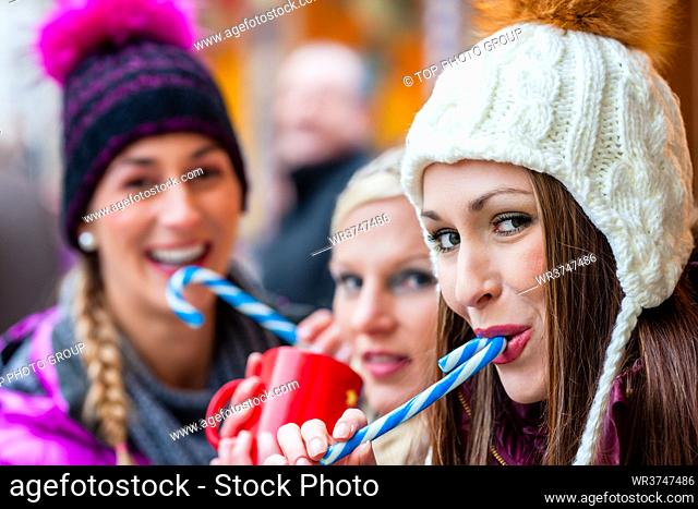 Women drinking mulled wine in mugs and eating candy sticks on German Christmas Market