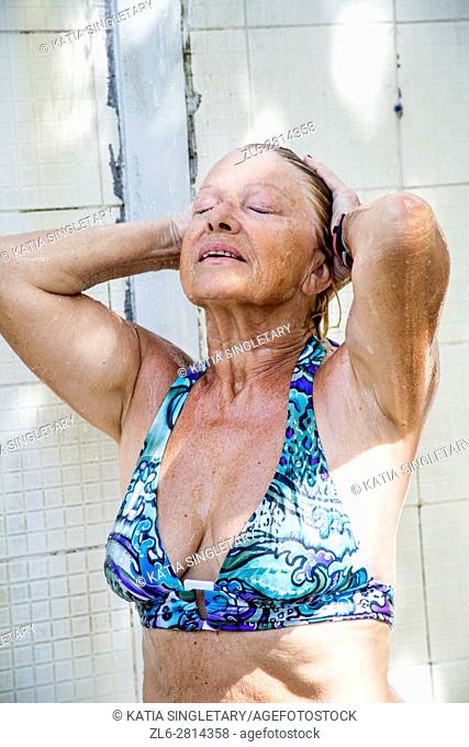Older retired senior caucasian woman showering at the beach in a blue bathing suit
