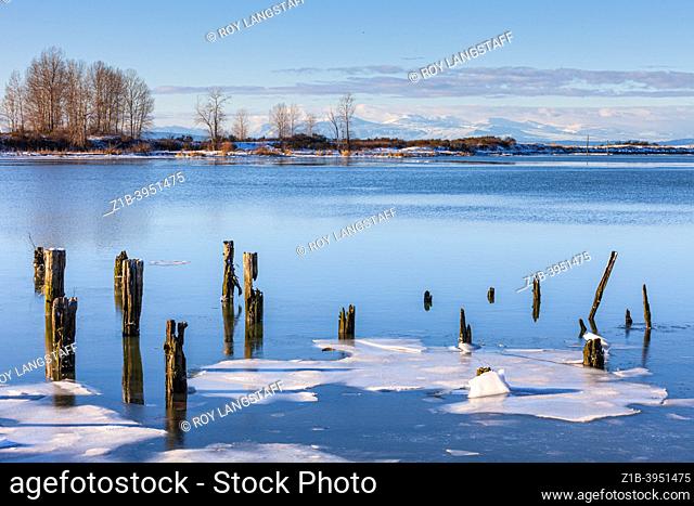 Sheets of ice among wooden pilings along the Steveston waterfront in British Columbia Canada with the mountains of Vancouver Island in the distance