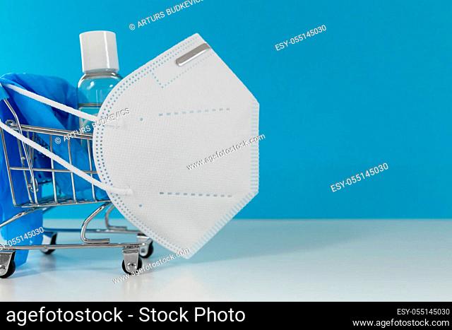 Shopping cart with facial mask hand sanitiser and blue gloves. Shopping and protection concept
