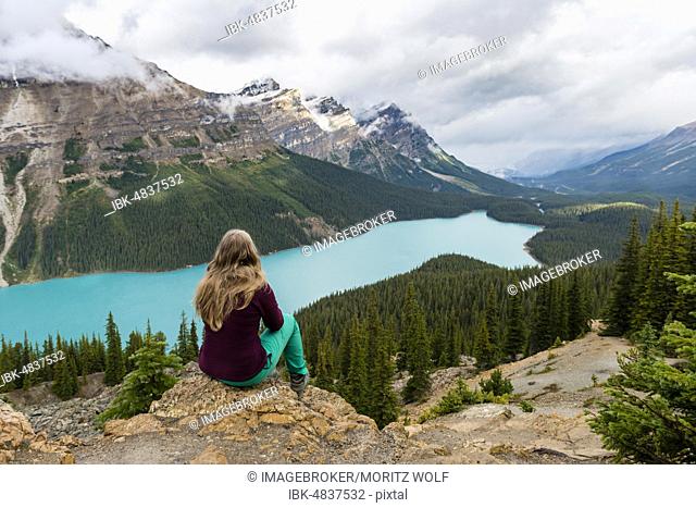 Young woman sitting on a stone looking into nature, turquoise lake, Peyto Lake, Rocky Mountains, Banff National Park, Alberta Province, Canada, North America