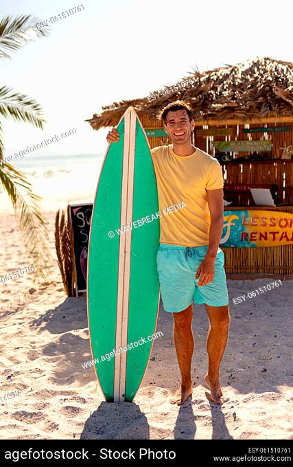 Young caucasian man holding surf board on beach