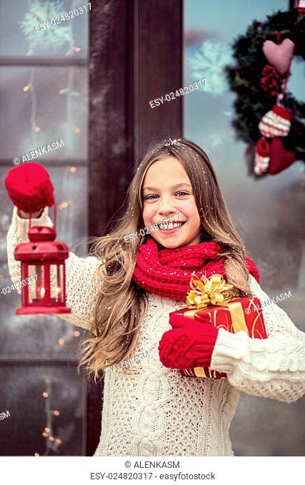 Child girl welcome guests and holding presents, snow weather, house door is decorated before Christmas