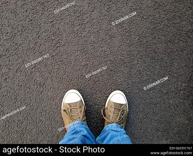 foot selfie or feet in canvas shoes standing on asphalt from personal perspective