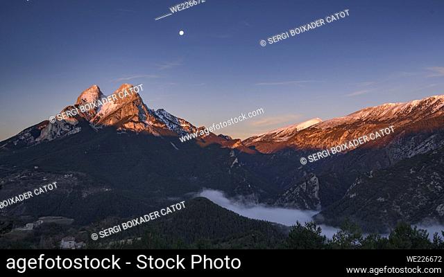 Winter sunrise in a snowy Pedraforca and the Full Moon over the mountain (Barcelona province, Catalonia, Spain, Pyrenees)