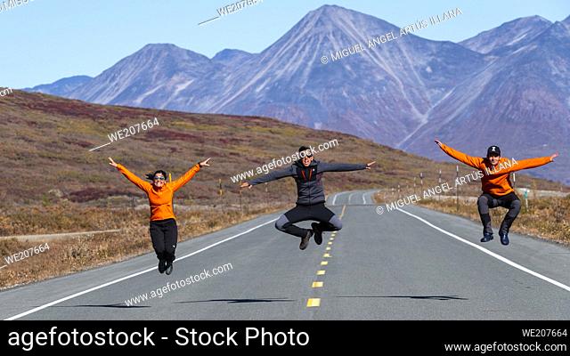 Two men and a woman run and jump on a road next to Kelsale Lake in the Yukon of Canada