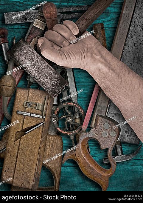 faded colors of a vintage woodworking tools and hand holding hammer on wooden bench