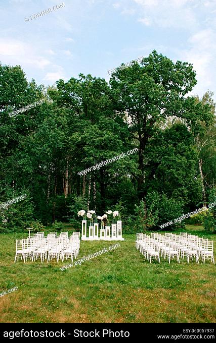 wedding ceremony in a beautiful garden. white chairs and mirrored tables. Glass vase with flowers calla lilies and white amaryllis