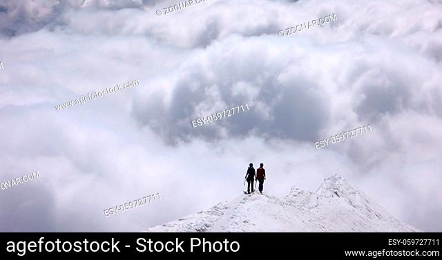 mountain climbers on a narrow snow ridge high above the clouds in the Alps of Switzerland near Pontresina in the Bernina mountain range