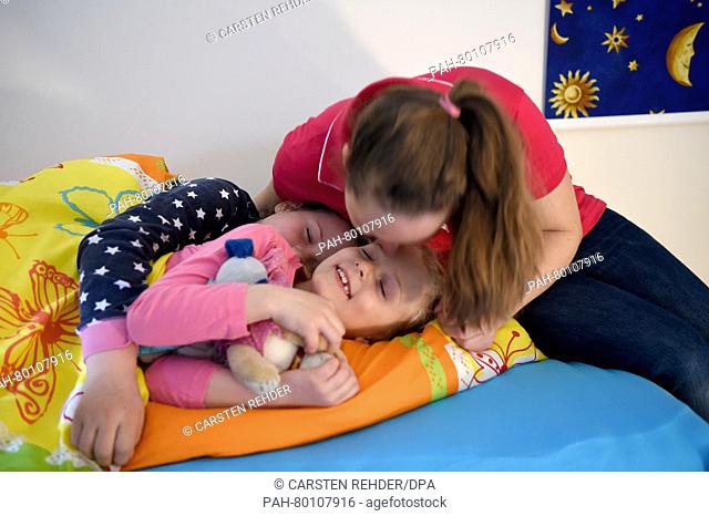 Sisters Skady-Lee (10) and Lucy-Mae (6) lie on a bed next to their mother Wiebke Ruedig at the night nursery at the Kapernaum daycare center in Flensburg