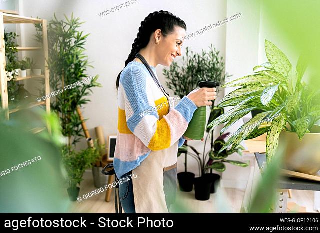 Female entrepreneur spraying water on plants in workshop