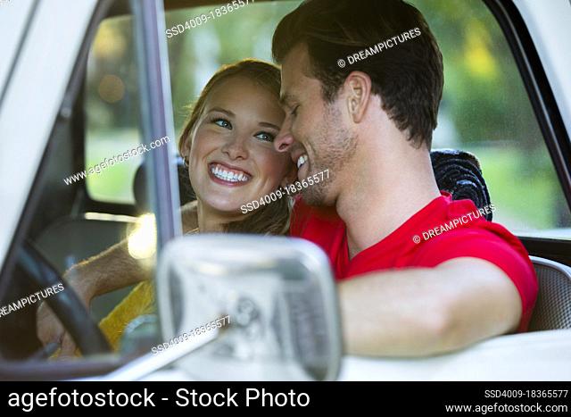 Young couple sitting in vintage pick up truck , guy with his arm around the girl while she looks over at him smiling