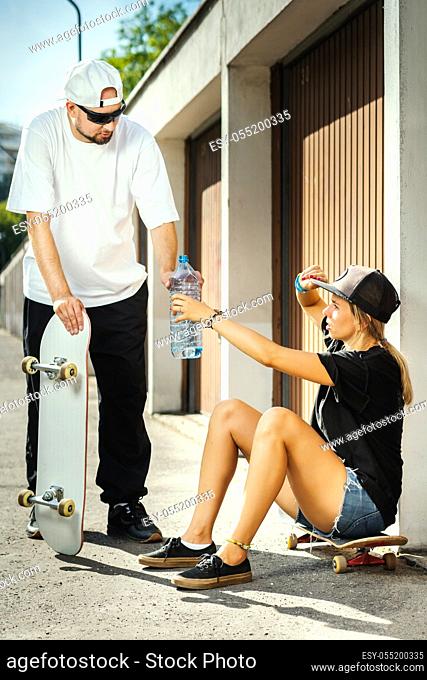 boy and girl on skateboards give themselves drinking water on a summer day
