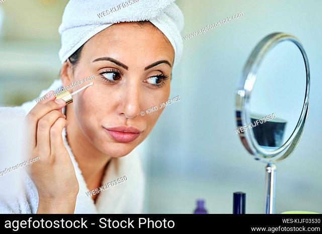 Beautiful woman applying beauty serum while looking in mirror at home