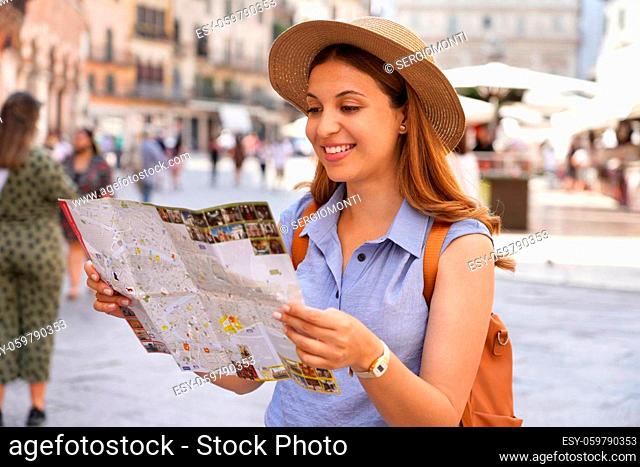 Happy young woman with a city map, straw hat and backpack travelling