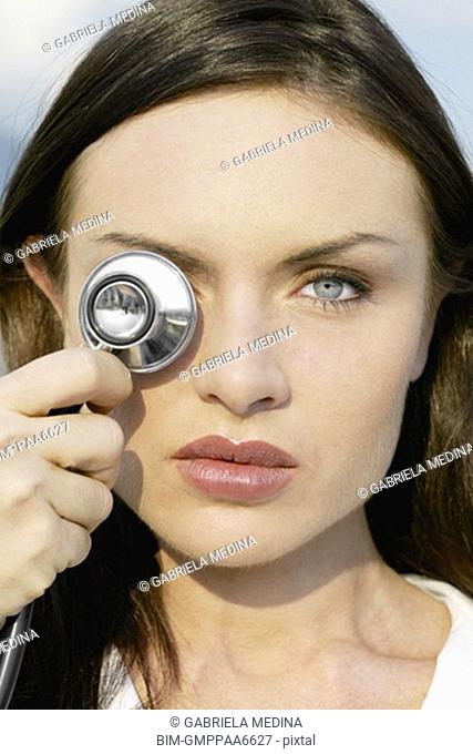 Close up of woman holding stethoscope over eye