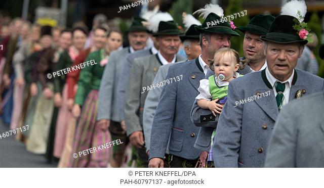 One and a half year old Maria, wearing a traditional Dirndl dress, is held by her father during the Assumption Day procession in Kochel am See, Germany