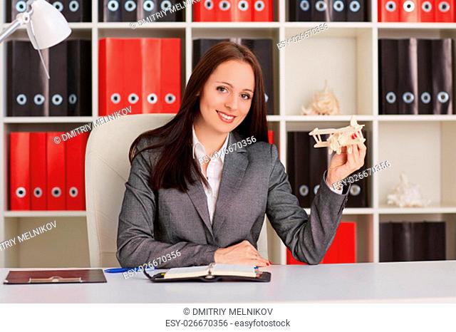 Businesswoman with a model of plane sits on a workplace in the office. Travel agency