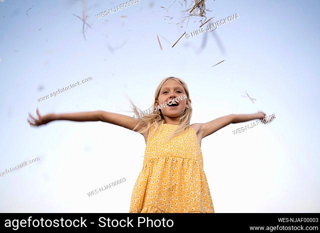 Happy girl throwing hay under clear sky