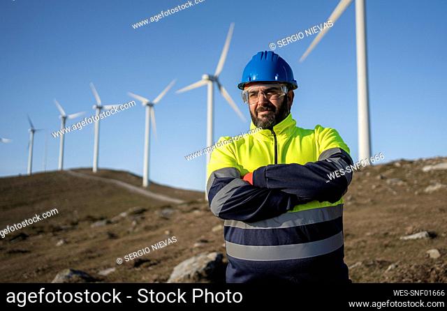 Mature engineer with arms crossed in front of wind turbines
