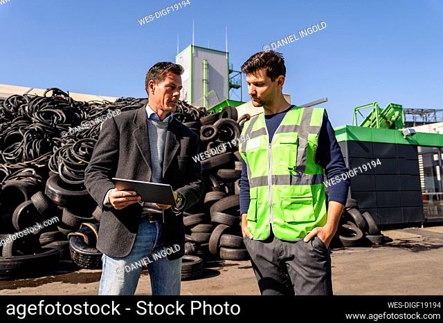 Businessman discussing over tablet PC with colleague in front of tires at recycling center