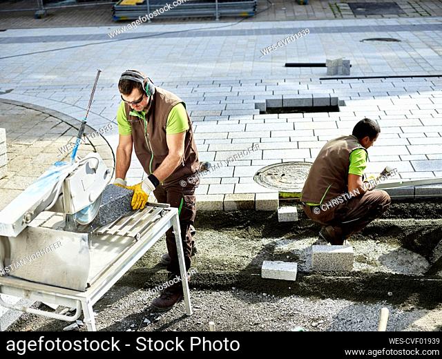 Paver cutting paving stone by coworker working in background