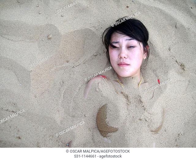 asian woman buried in sand on a beach