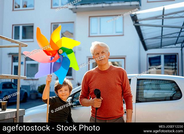 Smiling boy holding pinwheel toy by grandfather with charging plug