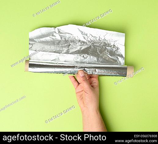 two female hands holds crumpled silver foil on a green background, close up