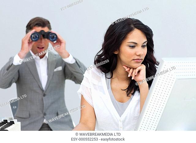 Mature businessman looking his colleague's computer through binoculars in the office