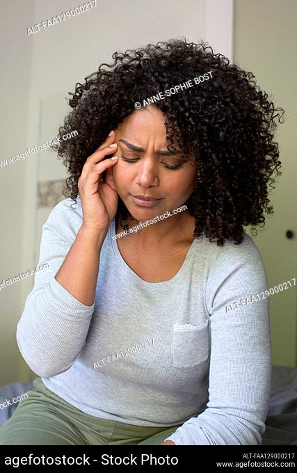 Woman suffering from headache while sitting in bedroom