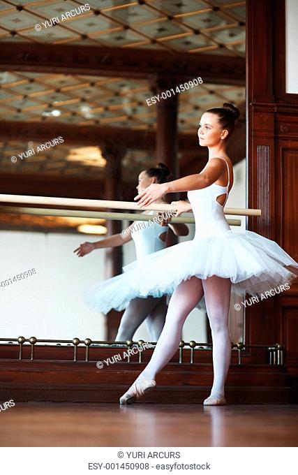 Full length of a young beautiful ballerina practicing with mirror in background
