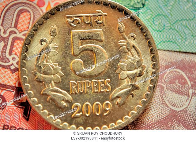 Indian Currency Coin of denomination Rs.5 placed on Indian currency note