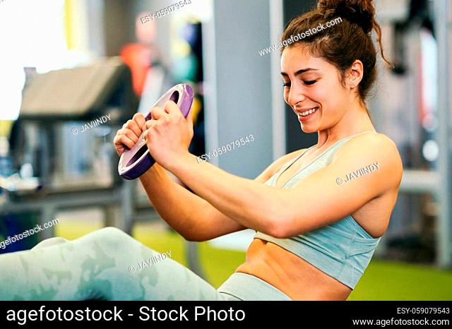 Sporty young female, wearing sportswear, on yoga mat doing situps with plate weights in gym. Fitness woman doing abs crunches
