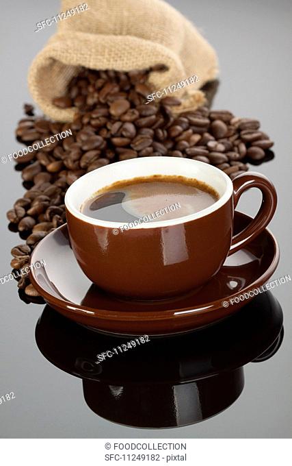 An espresso in a brown cup in front of a sack of coffee beans