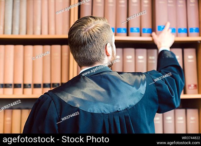 Young lawyer with robe ready to go to court grabs some books from library