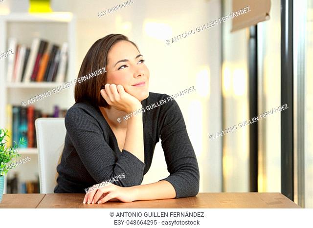 Satisfied homeowner thinking or draeming looking above sitting in a table at home