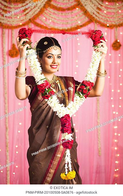 Bride in traditional South Indian dress holding a garland and smiling