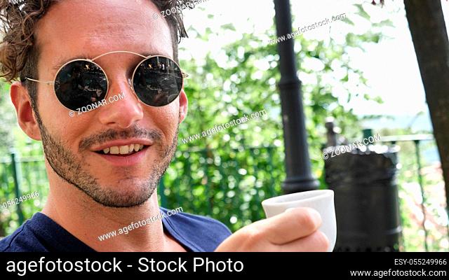 Portrait of smiling handsome man sitting at table with cup of coffee, outdoor on cafe or restaurant terrace, looking at camera smiling