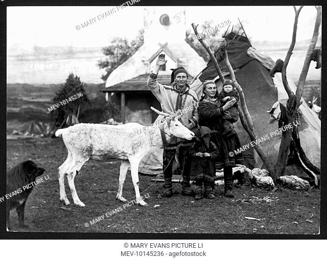 A Lapland man and woman with their two children, reindeer and dog, outside their tepee