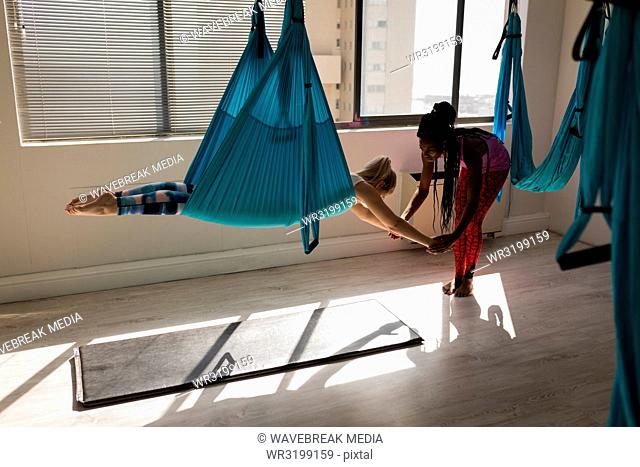 Female trainer assisting woman to exercise on swing sling hammock