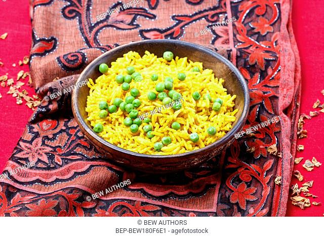 Indian cuisine, bowl of yellow rice with green peas on red background