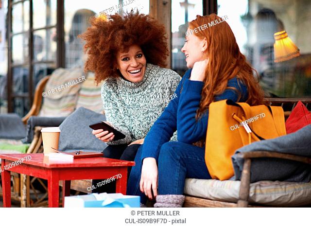 Friends at coffee shop using mobile phone laughing