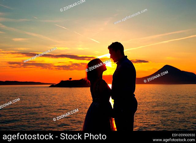 the bride and the groom standing on the on the beach of the Mamula island and holding hands at the sunset. High quality photo