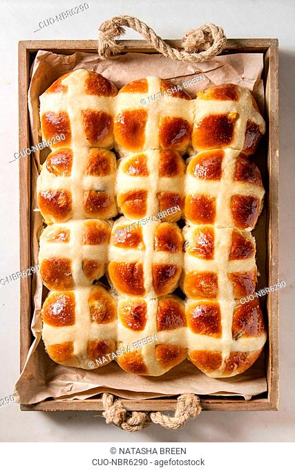 Homemade Easter traditional hot cross buns in wooden tray tray with baking paper over white marble background. Top view, space