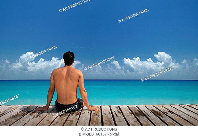 Caucasian man sitting on wooden dock at ocean
