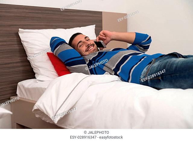 Young Man Lying On Bed And Having Fun On Phone In Bedroom